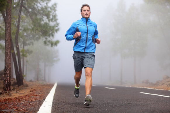 Man in light blue jacket running along wooded road